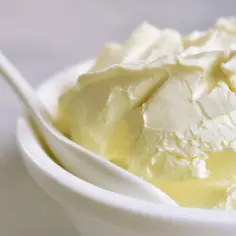 Kremowa masa w miseczce, idealna jako zamiennik mascarpone. Biała łyżeczka zanurzona w kremie.
