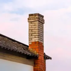 Ceglany komin na dachu z eternitu, na tle nieba.