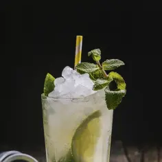 Orzeźwiający mojito drink ze spritem, lodem, limonką i miętą, z żółto-białą słomką.
