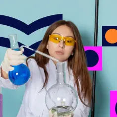 Dziewczyna w okularach ochronnych i białym fartuchu przeprowadza eksperymenty chemiczne z płynami w probówkach.