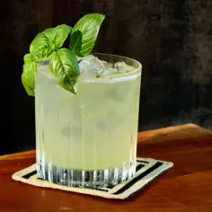 Orzeźwiający gin basil smash z listkami bazylii, podany na lodzie w szklance na drewnianym blacie.