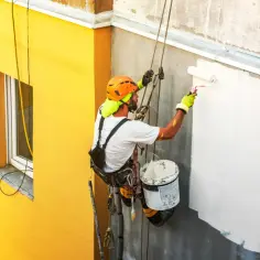 Pracownik wysokościowy maluje elewację. Zastanawiasz się, ile kosztuje pomalowanie elewacji? Sprawdź!