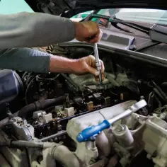 Mechanik pracuje przy silniku, używając klucza. Może to być związane z aplikacją dodatku do benzyny czyszczącego wtryski.