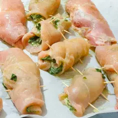 Soczyste roladki z kurczaka z piekarnika w sosie, nadziewane szpinakiem i serem, gotowe do pieczenia.