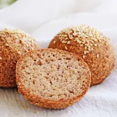 Trzy keto bułki posypane sezamem, jedna przekrojona na pół, na białym tle.