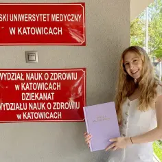 Uśmiechnięta studentka z pracą magisterską przed Śląskim Uniwersytetem Medycznym. Zastanawia się, ile zarabia pielęgniarka z magistrem.