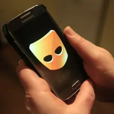 Dłonie trzymają smartfon z logo Grindr. Aplikacja ta służy do poznawania ludzi. Grindr co to? To popularny portal społecznościowy.