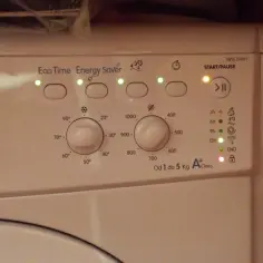 Panel sterowania pralki Indesit z podświetlonymi wskaźnikami i pokrętłami programów.