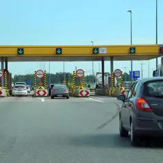 Kolejka samochodów na **autostradzie bursztynowej** przy bramkach poboru opłat. Zielone strzałki wskazują otwarte pasy.