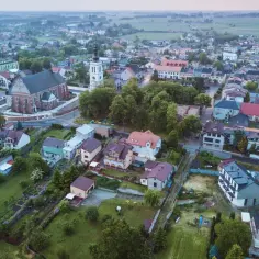 Widok z lotu ptaka na Uniejów, z kościołem i wieżą ratuszową w centrum. Miasto otoczone zielenią i polami.