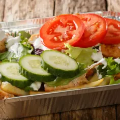 Kapsalon co to? Danie z kurczakiem, frytkami, sałatą, pomidorami i ogórkiem w aluminiowym opakowaniu.