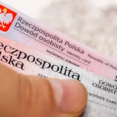 Dłoń trzyma polskie dowody osobiste, gotowe do wymiany. Widoczny orzeł i flagi UE.