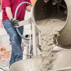 Robotnik wylewa chudy beton z betoniarki do taczki. Budowa w toku.