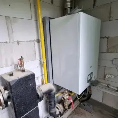 Biały piec na pellet Ferroli z żółtą rurą gazową i instalacją hydrauliczną.