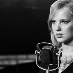Joanna Kulig w czarno-białym kadrze, przed mikrofonem, jak w jednym z jej filmów.
