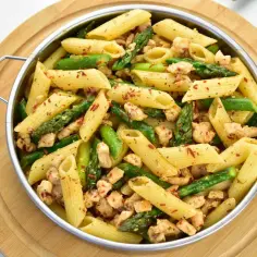 Makaron penne z kurczakiem i zielonymi szparagami w metalowej patelni.