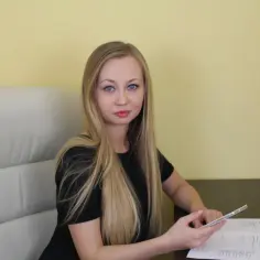 Kobieta z długimi blond włosami siedzi przy biurku, trzymając telefon.