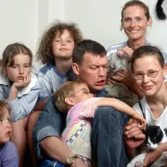 Olga Frycz z dziećmi i zwierzętami na kanapie. Wesoła rodzina, choć ojciec wygląda na lekko zirytowanego.