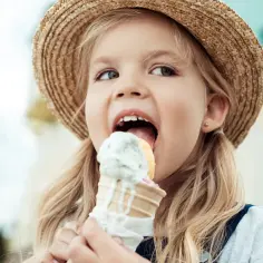 Mała dziewczynka w słomkowym kapeluszu zajada lody na patyku, które mogą pomóc na anginę.