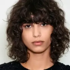 Kobieta z burzą ciemnych, kręconych włosów w stylu bob. Jej loki tworzą naturalną, swobodną fryzurę.