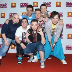 Siedmiu uśmiechniętych mężczyzn pozuje do zdjęcia. Wszyscy enej członkowie zespołu są w dobrych humorach.