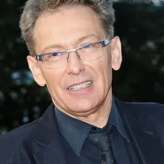 Piotr Rafalski, znany z roli w serialu "Klan", w czarnym garniturze i okularach.