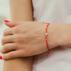 Czerwona nitka na nadgarstku, ozdobiona złotymi koralikami i cyrkonią, symbolizuje ochronę i szczęście.