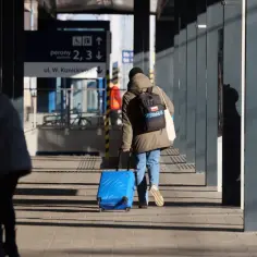 Osoba z niebieską walizką i plecakiem na dworcu. Czy to bagaż ponadwymiarowy w pociągu?