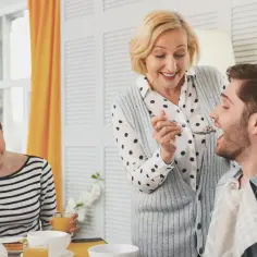 Matka karmi łyżeczką dorosłego syna, podczas gdy jego partnerka patrzy z irytacją.