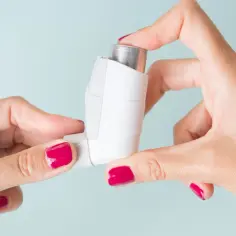 Dłonie z malinowym lakierem do paznokci trzymają inhalator, gotowy do użycia. To może być oxodil combo, by złagodzić objawy astmy.
