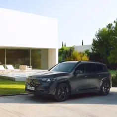 Ciemnoszary Mercedes GLB 200 stoi przed nowoczesnym domem z basenem i leżakami.