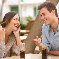 Uśmiechnięty mężczyzna opowiada dowcip, a kobieta śmieje się, bawiąc się włosami. Widać oznaki flirtu mężczyzny w jego spojrzeniu i gestykulacji.