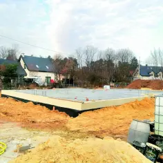 Płyta fundamentowa domu, której poziom zero jest lekko nad gruntem, otoczona piaskiem i materiałami budowlanymi.