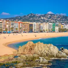 Słoneczna plaża w Lloret de Mar z kolorowymi budynkami i górami w tle. Wspaniałe lloret de mar atrakcje czekają!