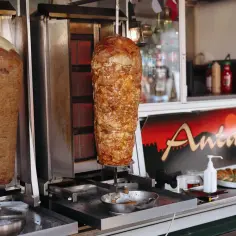 Dwa pionowe rożna z mięsem kebab, jeden z białą warstwą na górze, drugi z soczystym mięsem. Obok znak "Antalya".