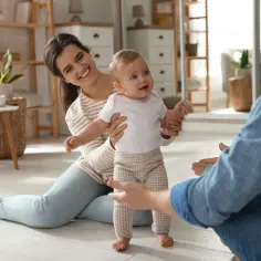 Rodzice zachęcają dziecko do pierwszych kroków. Uśmiechnięta mama i tata z otwartymi ramionami motywują malucha do chodzenia.