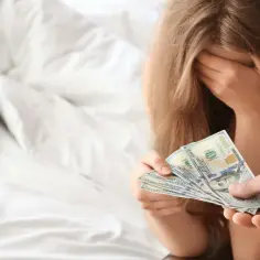 Kobieta z ręką na twarzy otrzymuje pieniądze, co sugeruje sytuację związaną z sutenerstwem.