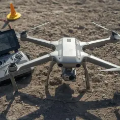 Szary dron i jego kontroler leżą na ziemi, gotowe do precyzyjnych **pomiarów dronem**. Na ekranie kontrolera widać mapę.