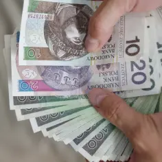 Dłonie trzymają stos polskich banknotów: 10, 20 i 100 złotych. To świadczenie wspierające punkty.