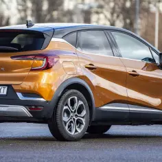 Pomarańczowy Renault Captur, idealny suv do 70 tys. zł, z czarnym dachem i eleganckimi felgami, prezentuje się na mokrej nawierzchni.