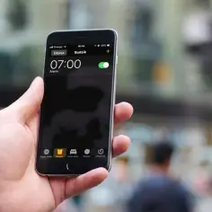Dłoń trzyma iPhone'a z włączonym budzikiem na godzinę 07:00.