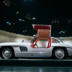 Srebrny Mercedes Gullwing z otwartymi drzwiami, prezentujący czerwone wnętrze. Ikona motoryzacji.