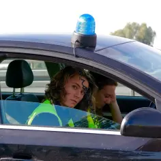 Młoda policjantka w kamizelce odblaskowej w radiowozie z niebieskim kogutem. Marzy, jak zostać podkomisarzem policji.