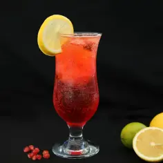 Orzeźwiający drink z granatem, ozdobiony plasterkiem cytryny, z owocami w tle.