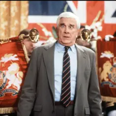 Leslie Nielsen w filmach, serialach i programach zawsze potrafił rozbawić. Tutaj w scenie z królewskimi sztandarami i trąbkami.