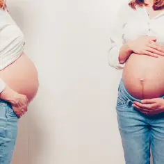 Dwa brzuchy w ciąży, jeden z profilu, drugi z przodu, oba w dżinsach i białej koszuli. Każdy kształt brzucha w ciąży jest unikalny.