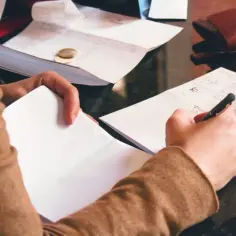 Osoba notuje na papierze, obok leżą rachunki i monety. Może to być przygotowanie do uzyskania gwarancji bankowej.