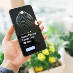 Dłoń trzyma iPhone'a z aplikacją Wallet, która ułatwia płatności. Technologia NFC w iPhone'ie sprawia, że transakcje są szybkie i bezpieczne.