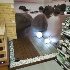 Nowoczesny taras z deski kompozytowej, otoczony kamieniami, z kulistymi lampami i widokiem na plażę z kamieniami.