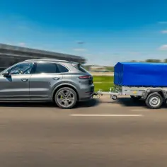 Szary SUV ciągnie przyczepę kempingową pod niebieską plandeką. Zastanawiasz się, ile kosztuje przerejestrowanie przyczepy kempingowej?